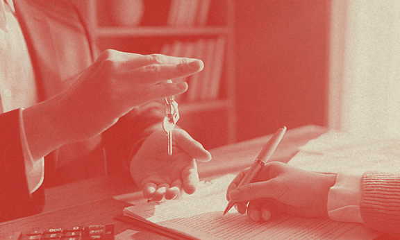 Bir insan, bir masanın üzerindeki elinden anahtar sarkıtmakta.