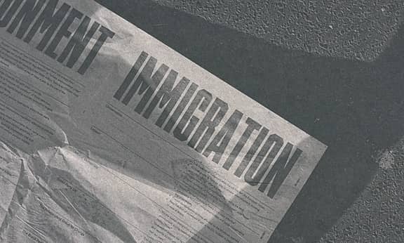 A newspaper's front page is seen laying on the street, with its main title writing "permanent immigration"